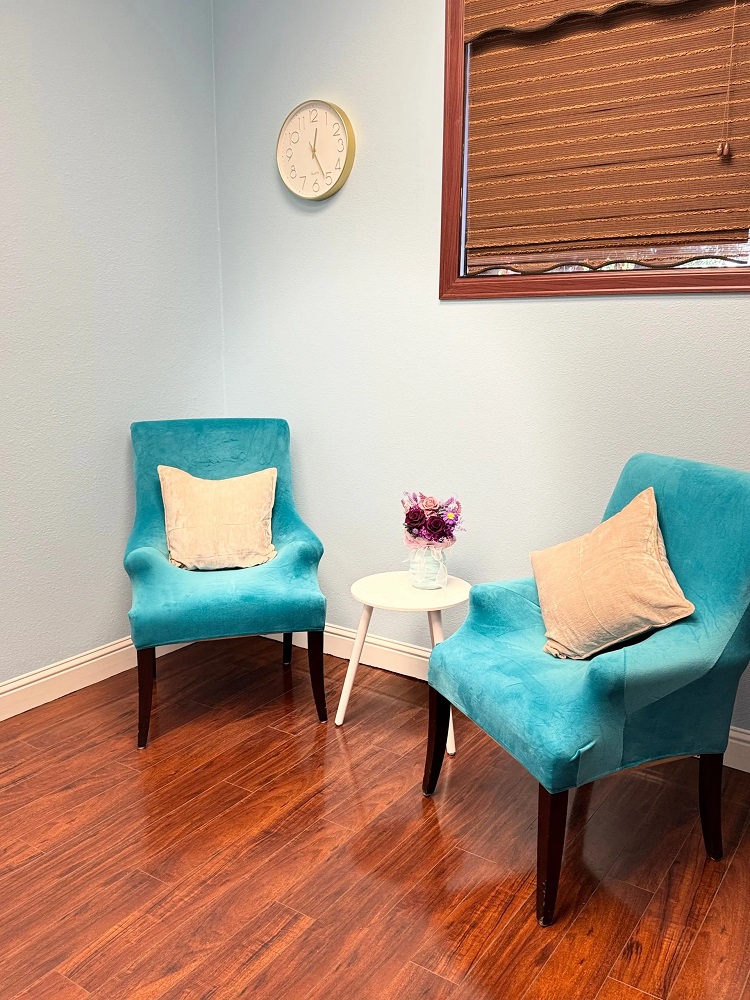 Two vibrant turquoise armchairs with white pillows arranged around a small white side table in a room with wood-style flooring