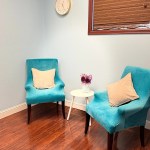 Two vibrant turquoise armchairs with white pillows arranged around a small white side table in a room with wood-style flooring