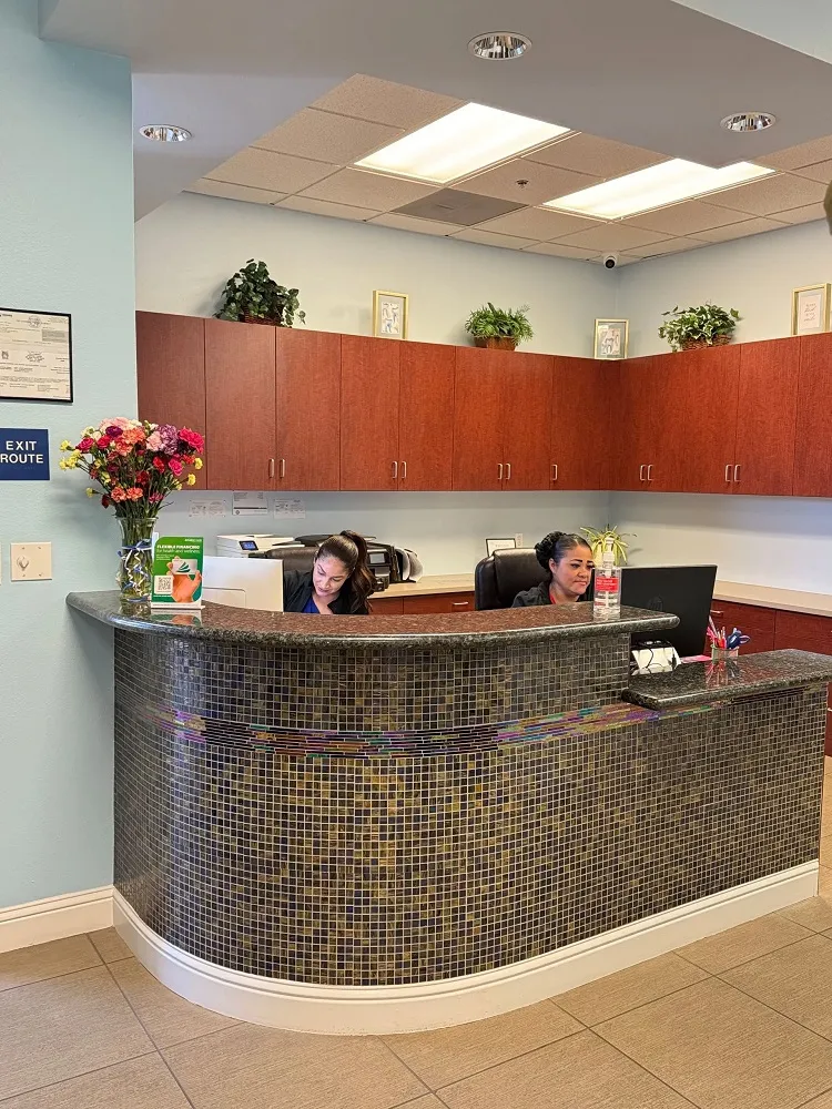 A curved, dark-tiled reception desk with a granite countertop, situated in front of wood-grain cabinetry and a bright office space