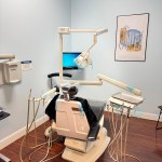 A dental operatory room featuring a professional patient chair, overhead lighting, and medical equipment against light blue walls