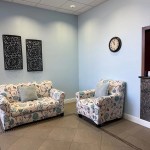 A bright waiting room with light blue walls, tiled floors, and two white sofas with a blue and pink floral pattern.