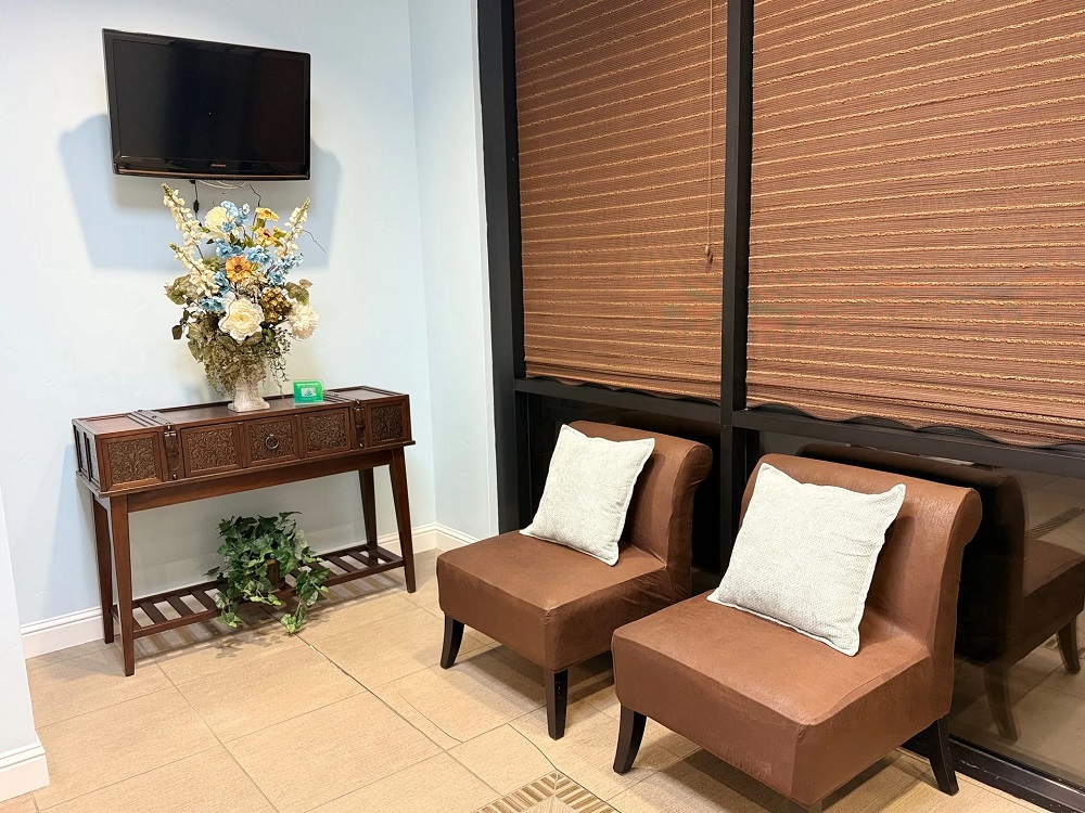 Two brown leather chairs with white pillows sit next to a wooden console table decorated with a large floral arrangement and a wall-mounted TV