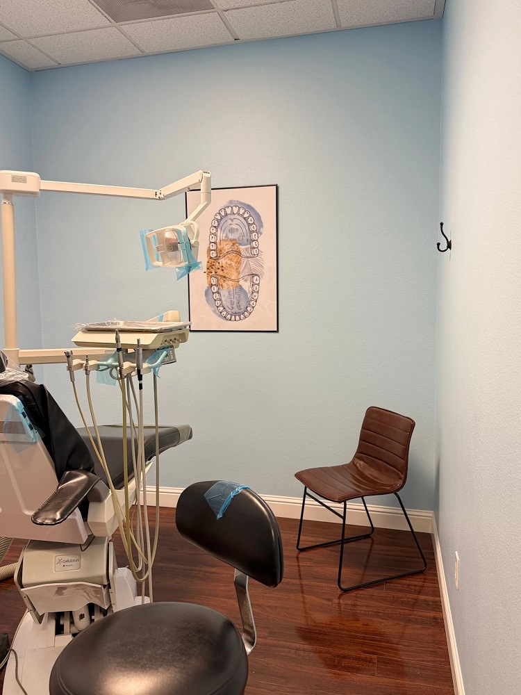 A side view of the dental exam room showing the patient chair and a brown guest chair against the wall