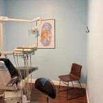 A side view of the dental exam room showing the patient chair and a brown guest chair against the wall