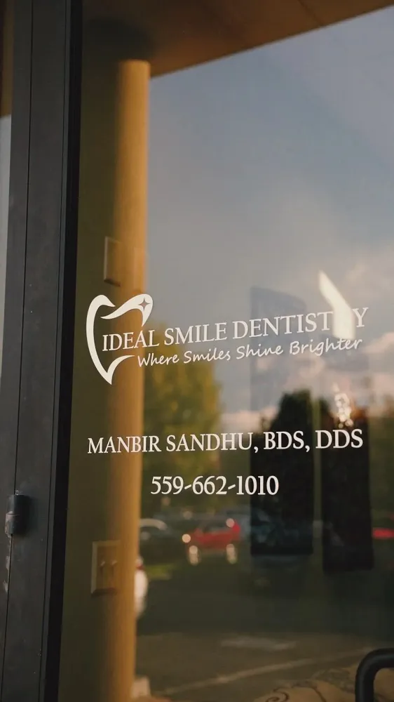 A vertical view of a glass door reflecting the sunset, featuring the logo and name of a dental office with contact information.