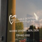 A vertical view of a glass door reflecting the sunset, featuring the logo and name of a dental office with contact information.